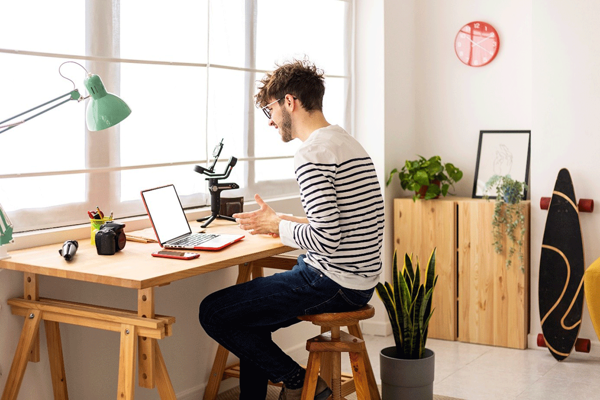 Ein junger Mann sitzt an seinem Schreibteisch vor dem Laptop.