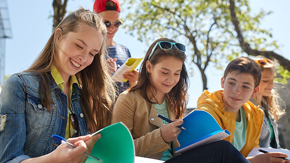 Sommerferienkurse bei der Schülerhilfe Schülerinnen und Schüler sitzen zusammen mit Heften in der Hand.